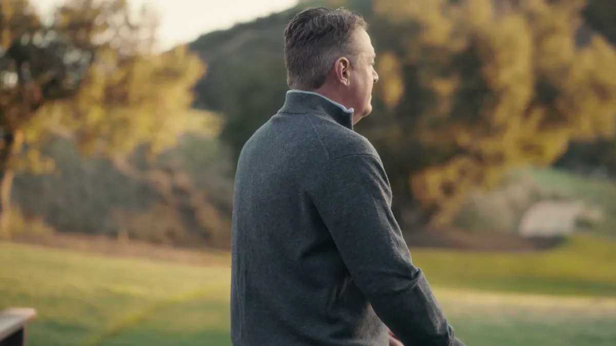 Keith Davidson attorney profile thumbnail. Shot from behind, a man in a dark quarter-zip pullover with a lawn and trees in front of him.