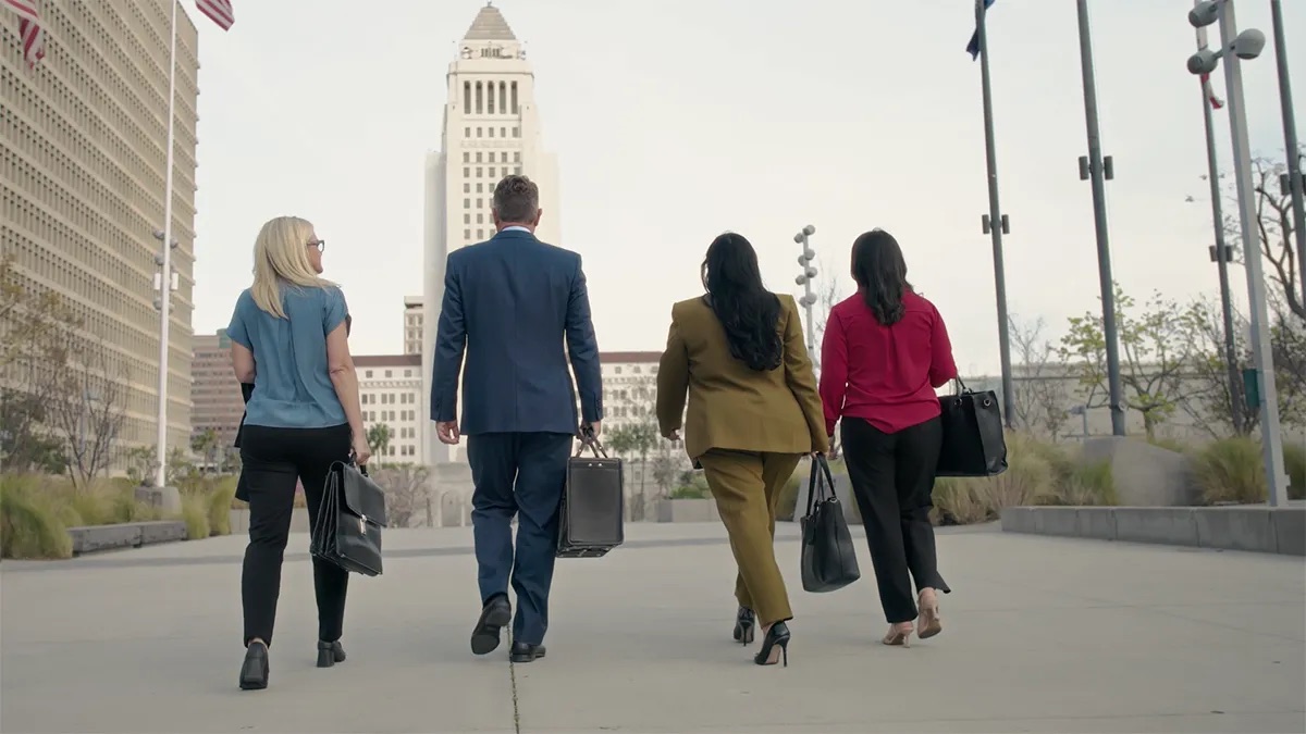 Four people crossing a broad plaza, LA City Hall directly in front of them