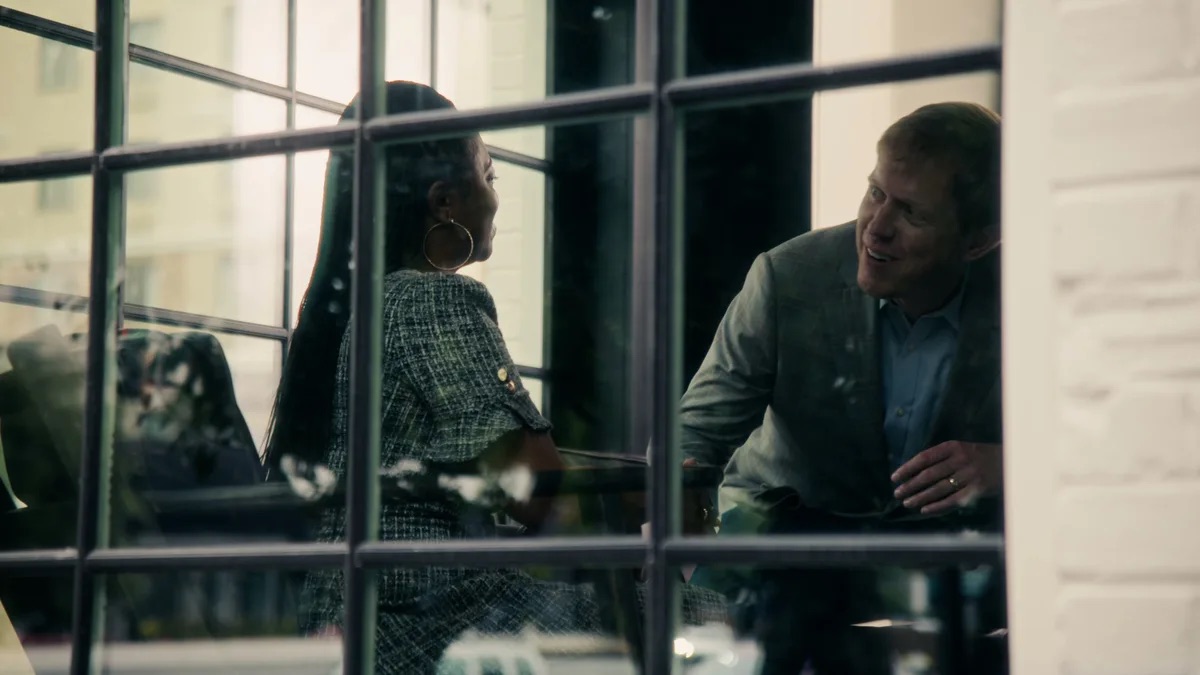Kevin Patrick Law practice area video thumbnail on car accidents. Shot through the window frames from outside, a woman and a man sit talking at a table inside.