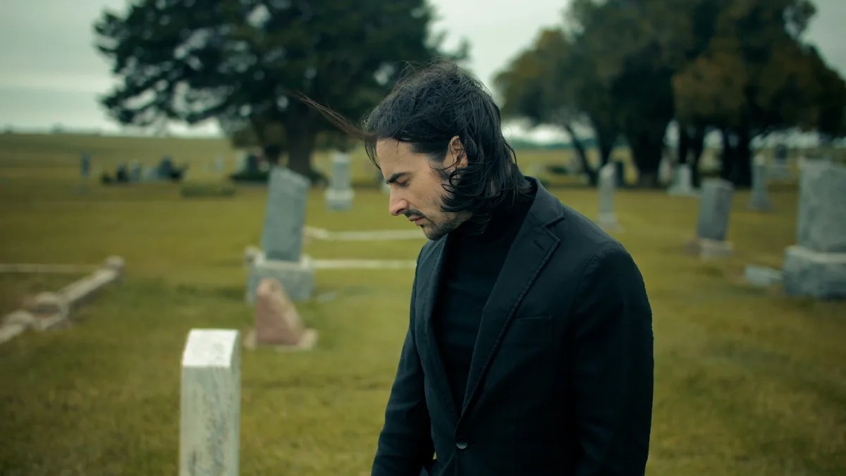 Kevin Patrick Law practice area video thumbnail on wrongful death. A man in a dark suit stands with his head down in a cemetery, headstones and trees behind him.