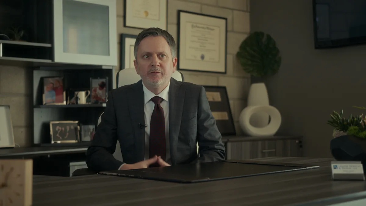 Lessem, Newstat & Tooson practice area video thumbnail on mental health. An attorney in a gray suit and maroon tie at a desk, framed diplomas on the wall, photos and a mug on a shelf.