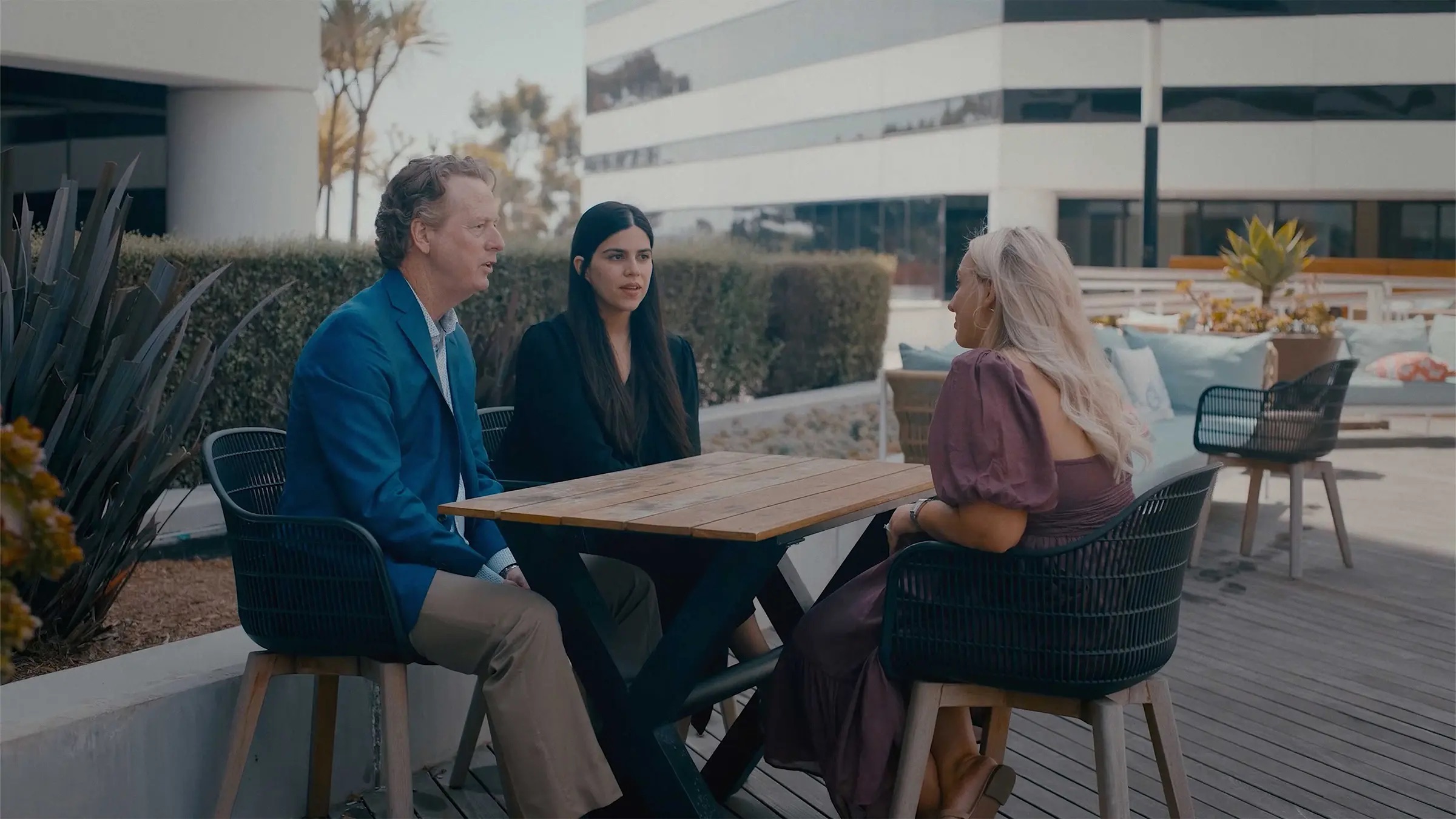Three people sitting at an outdoor table, one speaking while two listen