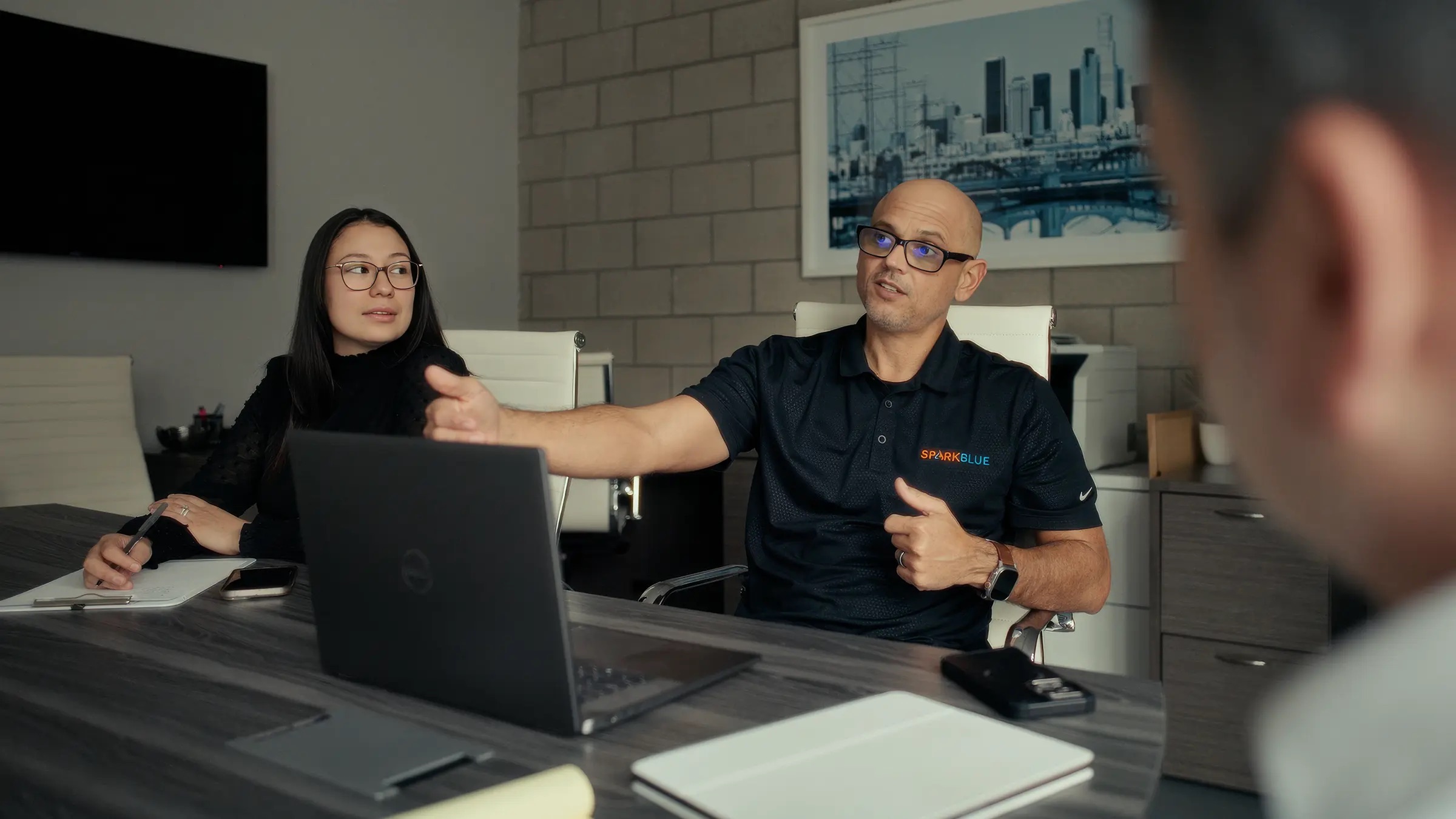 A man in a SparkBlue polo gesturing across a table while a colleague takes notes